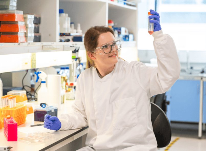 a scientist in the lab holding up and looking into a test tube