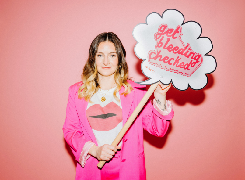 Lydia holding a sign that says 'get bleeding checked'