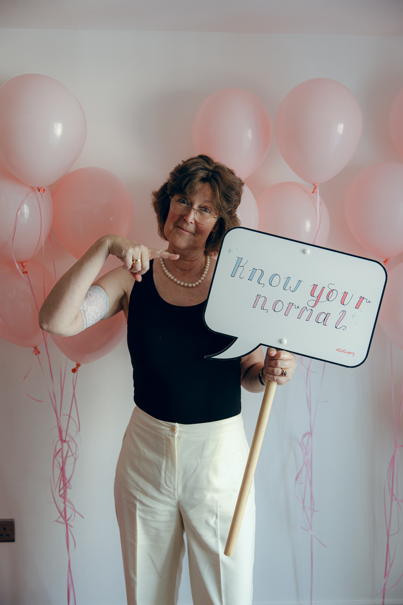 Photo of Ann Russell at Get Lippy event pointing to sign that says 'now your normal'