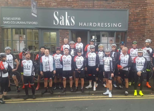 Group photo of people outside Saks hairdressing shop, Knutsford, wearing Saks tshirts and cycling helmets.