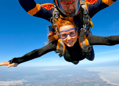 Photo of someone skydiving, looking at camera with their arms outstretched. 