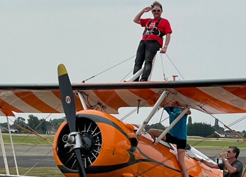 Photo of person on top of small aircraft wings looking at camera and saluting. 