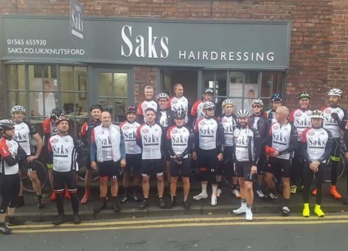 Group photo of people outside Saks hairdressing shop, Knutsford, wearing Saks tshirts and cycling helmets.